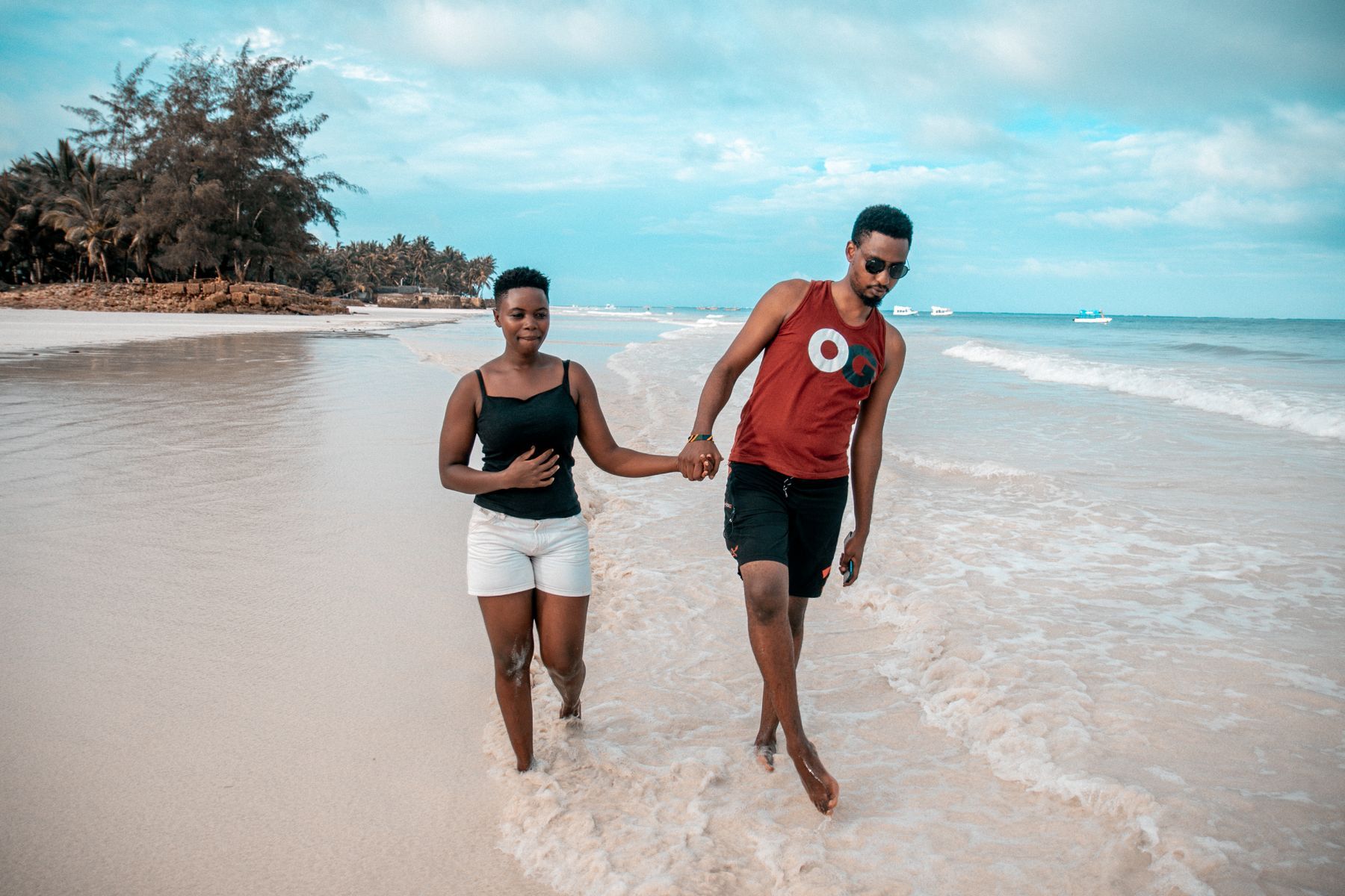 A couple walking hand in hand through the surf on a white-sand beach in Kwale, Kenya