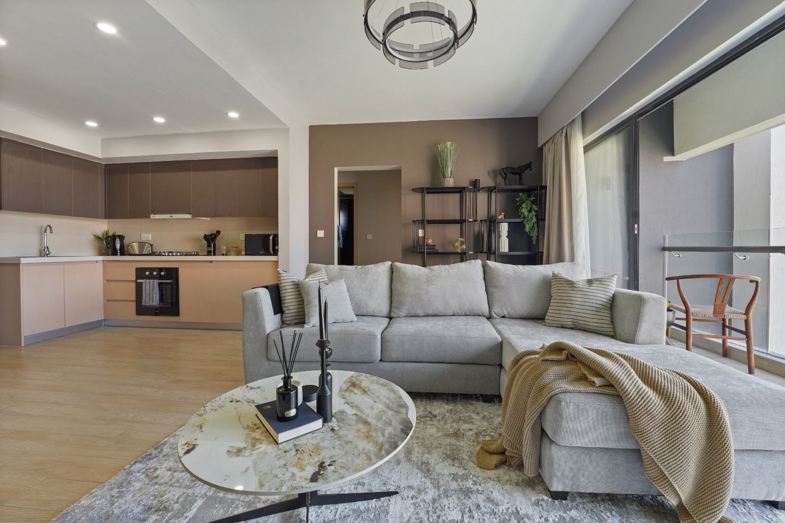 Furnished open-plan living room with a grey L-shaped sofa, marble coffee table and fitted kitchen